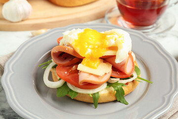Tasty brunch. Poached egg, ham, tomato, arugula and bun on white marble table, closeup