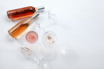 Bottles of delicious rose wine and glasses on white wooden table, flat lay. Space for text