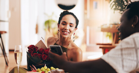 Couple, phone and roses with dinner in home with smile, gift and surprise with mobile app for romance, People, man and woman with interracial love, bouquet and social media on valentines day date