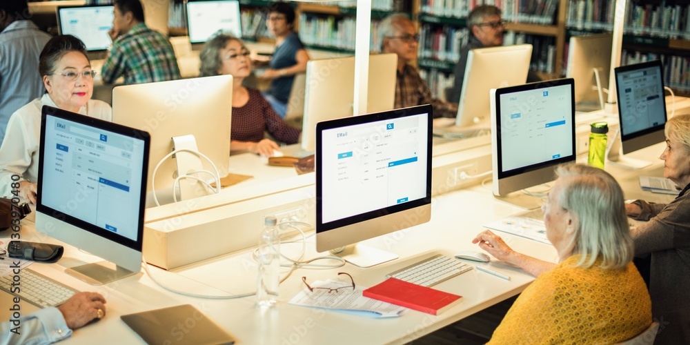 Poster People using computers in a library. Seniors engaged in learning. Library computers, learning, and engagement. Diverse group focused on technology and education. Senior students in computer class.