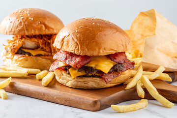 Juicy burgers with melted cheese and crispy bacon served with golden fries on a wooden board