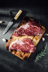 Fresh Raw Ribeye Steak on Wooden Cutting Board with Knife and Garlic Close-up