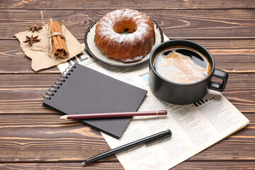 Cup of coffee with cake, cinnamon, notebook and newspaper on wooden background