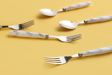 Stylish spoons and forks on yellow background