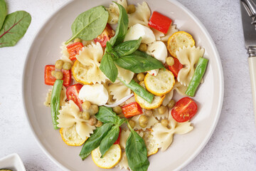 Plate of tasty pasta salad with peas and basil on white background