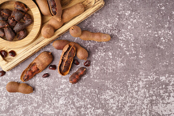 Wooden board and bowl of tasty tamarinds on grey background