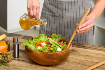 Woman adding olive oil into bowl with tasty salad at table in kitchen