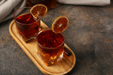Wooden tray with glasses of Old Fashioned Cocktail and dried orange slices on grey grunge background