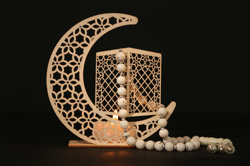 Decorative crescent with burning candle and prayer beads for Ramadan on table against dark...