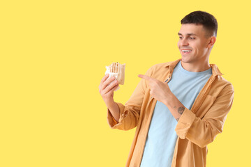 Handsome young man pointing at tasty doner kebab on yellow background