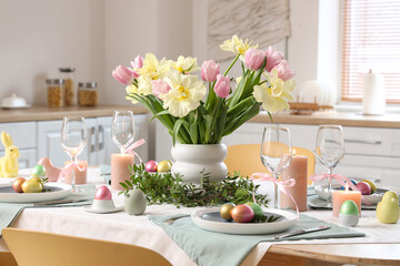 Festive Easter table setting with vase of flowers, cutlery, napkins and painted eggs in kitchen
