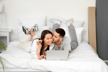 Fototapeta premium Young couple with keys and laptop video chatting in bedroom on moving day