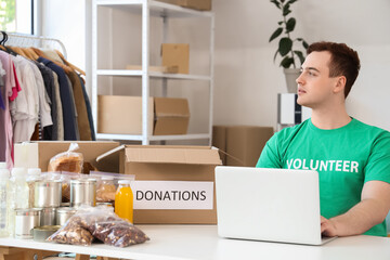 Male volunteer with food donations using laptop at table in center