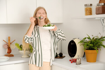 Young woman eating salad with feta cheese in kitchen