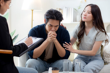 Young asian couple experiencing marriage counseling, wife comforting partner while talking with...