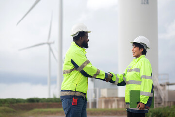 Two young engineer handshake about agreement of success renewable in wind turbines farm, renewable...