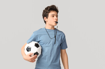Teenage boy with soccer ball and whistle on grey background