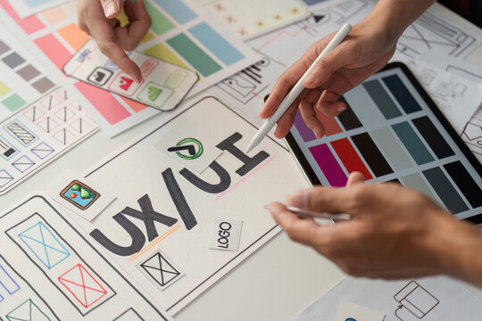 UXUI Design and Collaboration. Creative professionals engaged in user experience and interface design brainstorming on a table full of sketches and wireframes.