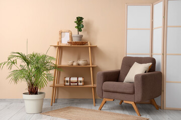 Interior of room with folding screen, armchair and shelving unit near beige wall