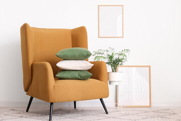 Comfortable armchair with stack of pillows near white wall