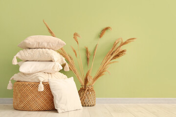 Wicket basket with stack of pillows and pampas grass near green wall
