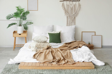 Cozy bed with soft pillows and crumpled blanket in interior of light bedroom