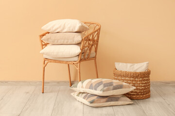 Wicker armchair with stack of pillows and basket near beige wall
