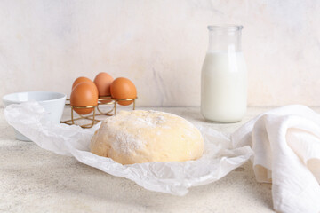 Baking paper with fresh raw dough, holder of eggs and bottle of milk on white background
