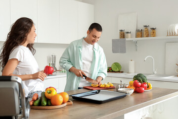 Young man cutting bell pepper with his wife in kitchen