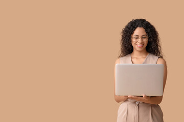 Young African-American businesswoman with modern laptop on brown background