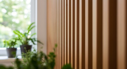 Wooden panel with vertical slats and green plants in a bright interior setting during the day, Close-up shot of a light brown vertical slatted wood wall, slightly out of focus, with blurred greenery