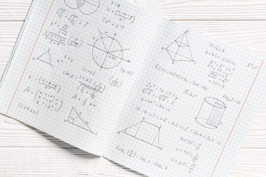 Copybook with handwritten maths formulas on white wooden background