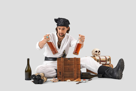 Young pirate with treasure and rum on light background