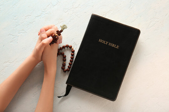 Hands of praying woman with rosary beads and Holy Bible on light background