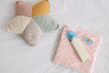 Bottle of baby milk formula, pacifier, plaid and cushion on light bed