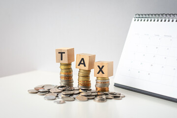 Tax word on wood blocks on top of coins with calendar at the background.