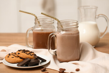 Mason jars of sweet chocolate milk and plate with tasty cookies on wooden table in kitchen