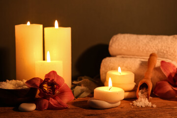 Spa composition with burning candles and orchid flowers on dark wooden table