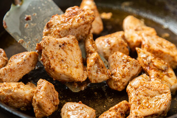 Chicken fillet pieces are fried in a frying pan in sauce and spices and turned