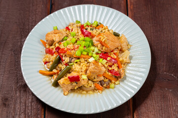 On a wooden table in a plate there are vegetables stewed with bulgur