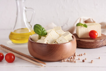Bowl with pieces of tofu cheese on white wooden background