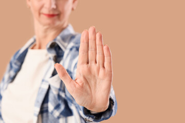Mature woman showing STOP gesture on beige background, closeup. Rules concept