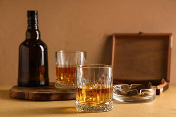 Bottle and glasses of cold rum on table against beige background. Closeup