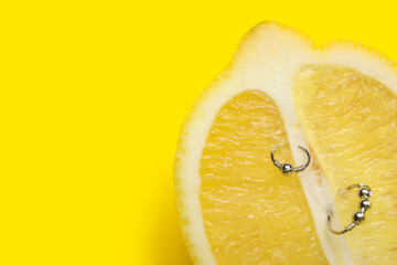 Half of lemon with piercing on yellow background, closeup