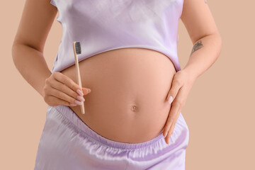 Pregnant woman with tooth brush on beige background, closeup