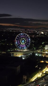 Vertical aerial view orbiting the ferris wheel of Aztlan Park, night in CMDX