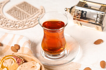 Glass of tasty Turkish tea with sweets, crescent and fanoos on white grunge background. Ramadan...