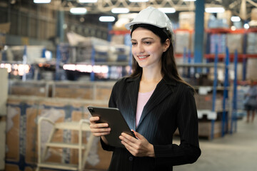 A woman wearing a hard hat and a black suit holding a tablet. She is smiling and she is happy