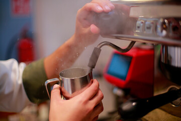 Barista heats up milk in the coffee machine to prepare a cappuccino