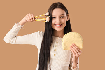 Teenage girl with makeup brushes and cosmetic bag on beige background